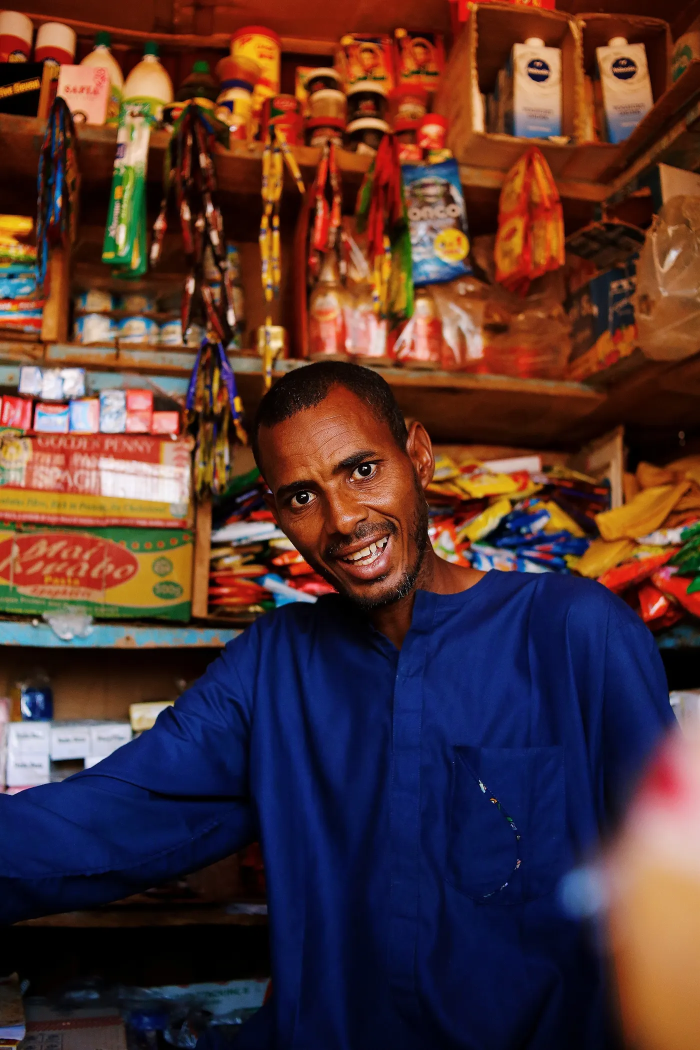 A shopkeeper smiling inside his stocked shop